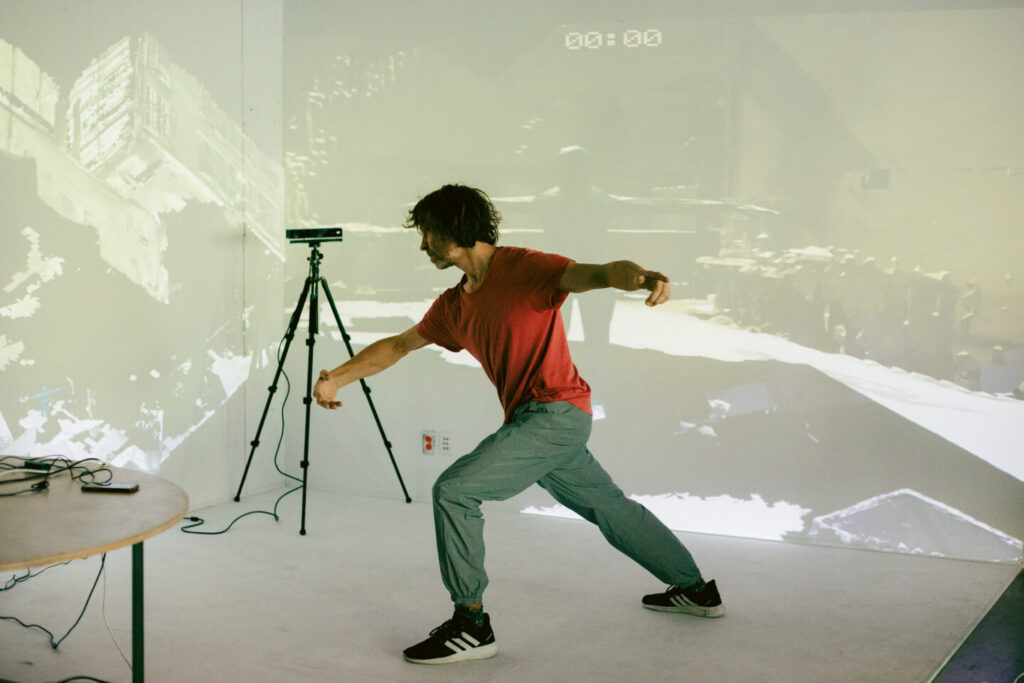 An artist moving through an immersive space with black-and-white video projections, in front of a camera mounted on a tripod.